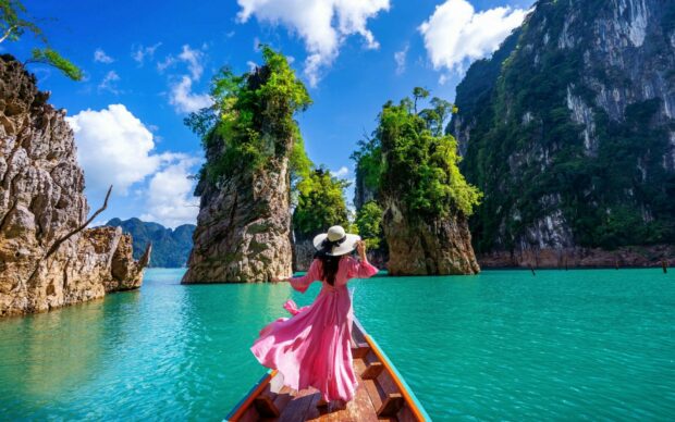 A woman in pink dress exploring Thailand nature with limestone cliffs and turquoise water in sight
