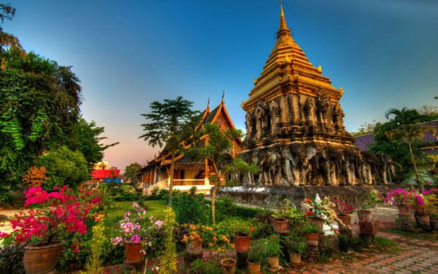 Ancient temple with elephant sculptures and colorful flowers in Thailand garden