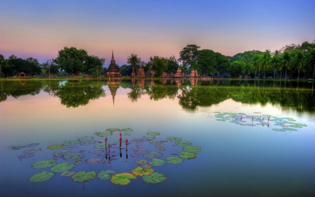 Ancient Thai architecture reflected in lake with lotus leaves at sunset in Thailand
