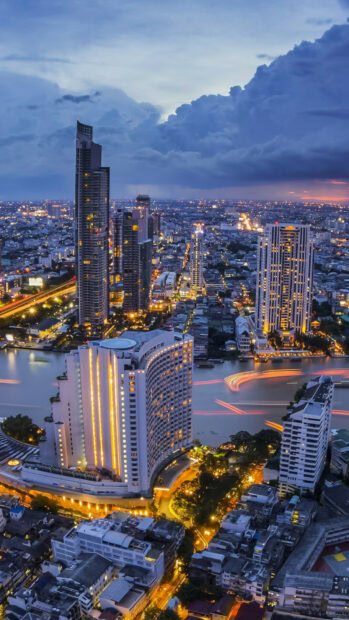 Cityscape of Thailand with illuminated skyscrapers and river at dusk in Thailand