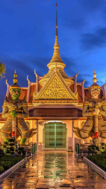 Two giant statues guarding a Thai temple with intricate architecture in Thailand at dusk
