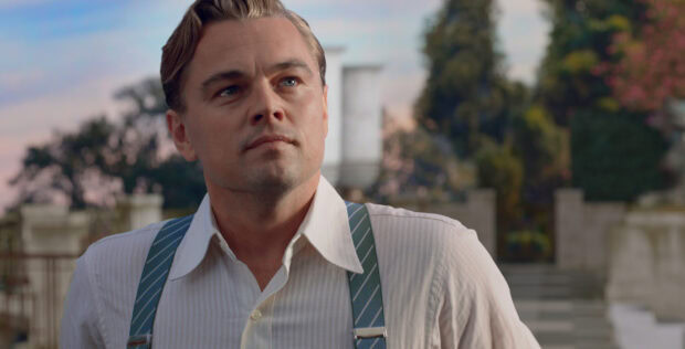 A man with suspenders stands outside a large estate in The Great Gatsby scene