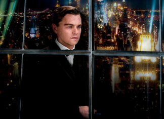 A man in a suit looking out the window over a cityscape at night from The Great Gatsby