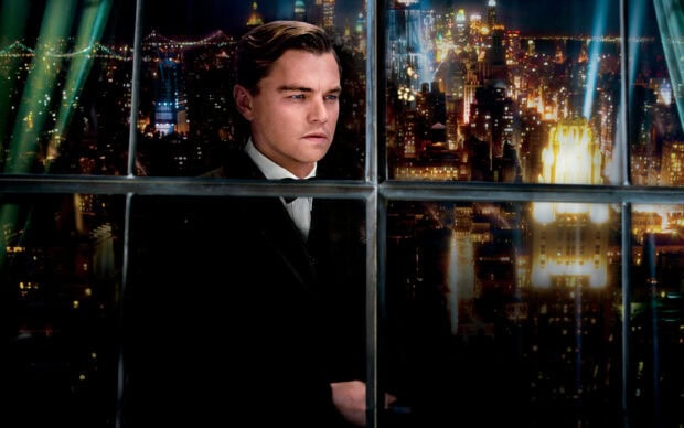 A man in a suit looking out the window over a cityscape at night from The Great Gatsby
