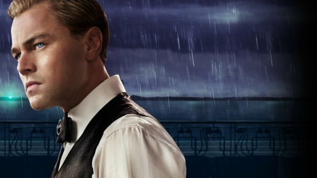 A close up of a man representing Gatsby standing in the rain by the water at night