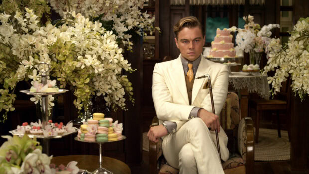 A man in a white suit sitting in a decorated room with flowers and desserts from The Great Gatsby