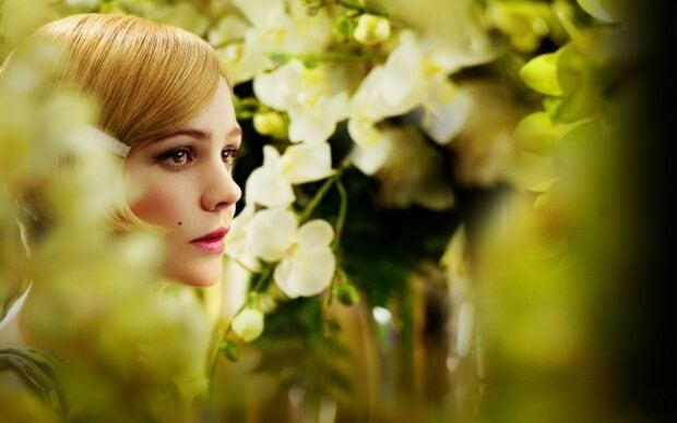 A close up of Gatsby character surrounded by white flowers in a soft focus setting