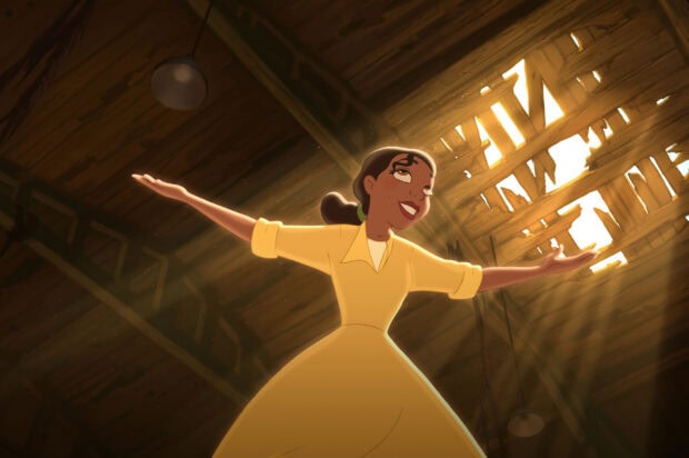 A joyful young woman in a yellow dress standing with arms open under sunlight streaming through a broken roof