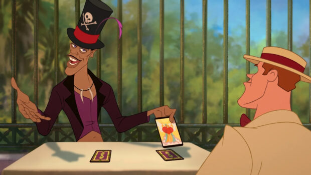 A man wearing a top hat shows tarot cards while talking to another man at a table in an outdoor setting