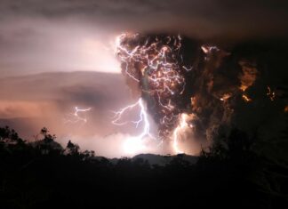 A dramatic thunderstorm with lightning illuminating dark clouds over a forested landscape