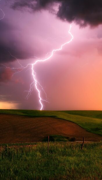 A striking thunder bolt flashes across the colorful sky over the open field