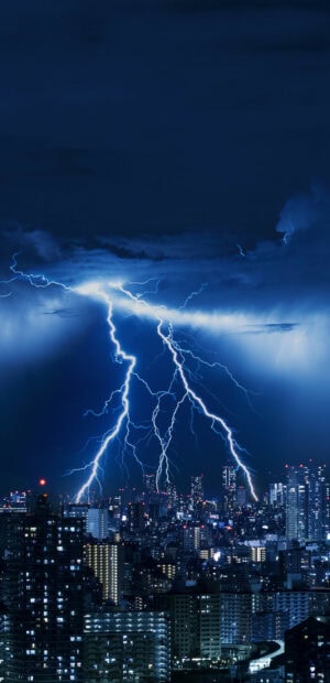 Lightning striking multiple times over a city skyline during a thunderstorm at night