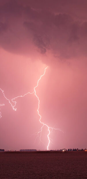 A powerful thunder bolt striking over a flat landscape during a stormy night