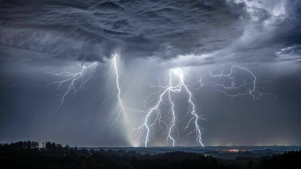 Lightning bolts striking over a dark stormy landscape with thunder clouds