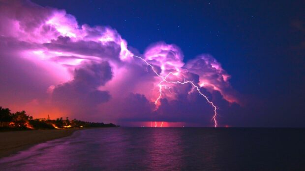 Lightning striking over a beach with thunder clouds illuminating the night sky