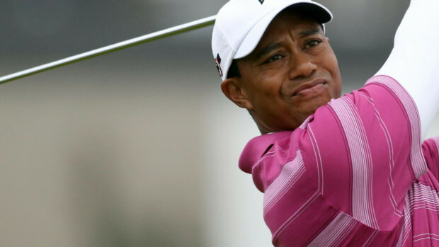 Tiger Woods focused during a golf swing in a pink striped shirt