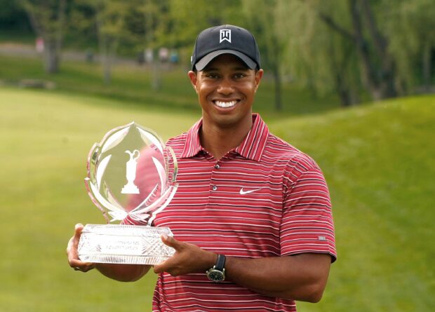 Tiger Woods holding a crystal golf trophy in a red striped shirt on a golf course