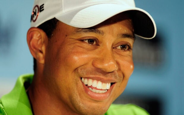 Tiger Woods wearing a white cap and green shirt smiling warmly in a close up shot