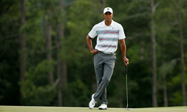 Tiger Woods standing on the golf course holding a putter wearing a white cap and striped shirt