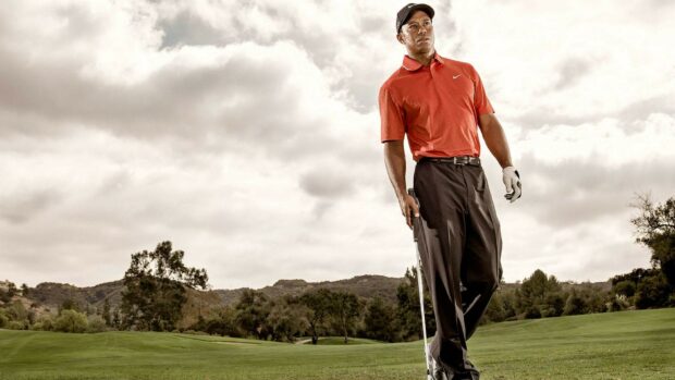 Tiger Woods standing on the golf course wearing a red shirt and holding a golf club