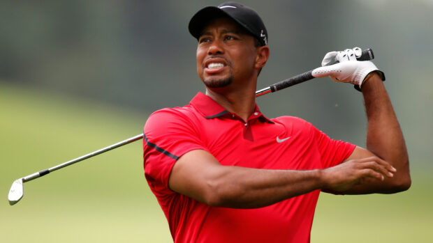 Tiger Woods wearing a red shirt swinging a golf club on the golf course