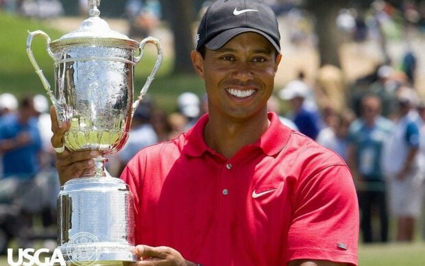 Tiger Woods holding a trophy in a red shirt smiling during a golf tournament