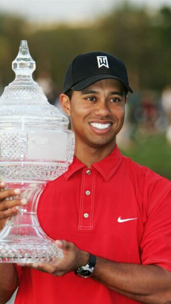 Tiger Woods holding a large trophy with a bright smile in a red shirt