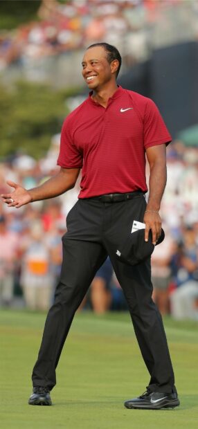Tiger Woods smiling on golf course wearing red shirt and black pants
