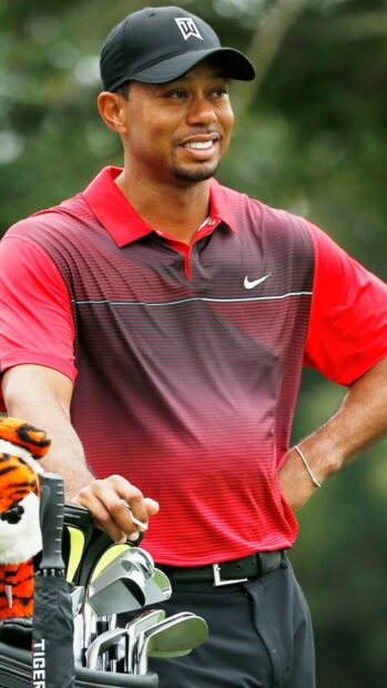 Tiger Woods standing by golf clubs wearing a red shirt and cap on the golf course