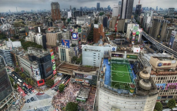 A busy Tokyo cityscape panorama with high rise buildings and a rooftop soccer field in view