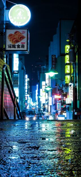 Nighttime Tokyo street scene with glowing signs and wet reflective pavement in Japan