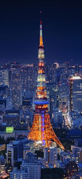 Tokyo Tower lit up in vibrant colors in Tokyo Japan at night with city buildings surrounding it