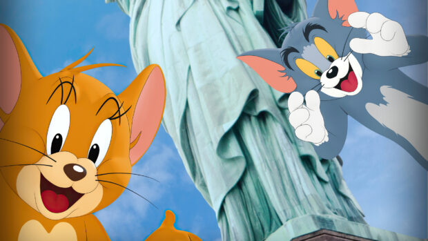 Tom and Jerry are happily posing in front of the Statue of Liberty with a bright blue sky background