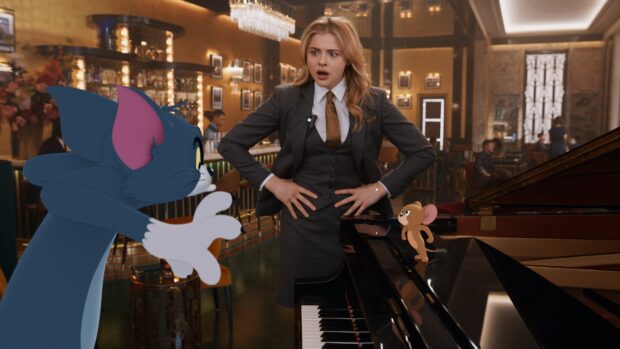 A surprised woman stands between Tom and Jerry near a piano in a luxurious room