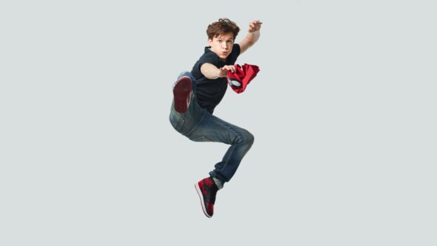 Tom Holland jumping and holding a red mask while wearing jeans and sneakers