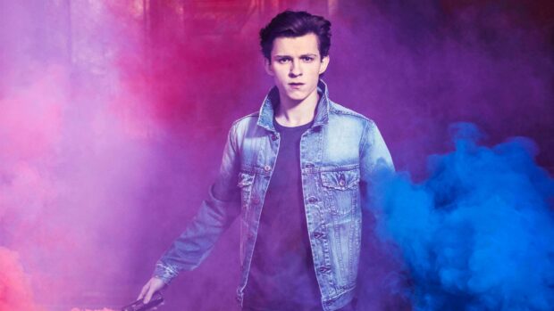 Tom Holland standing in a denim jacket surrounded by colorful smoke with a serious expression