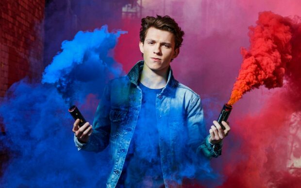 Tom Holland holding blue and red smoke grenades wearing a denim jacket