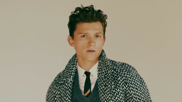 Tom Holland wearing a patterned coat and tie with a serious expression
