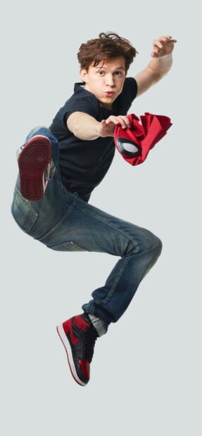 Tom Holland jumping while holding a red spider mask in a dynamic pose