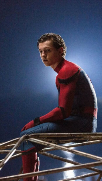 Tom Holland sitting in his superhero suit looking thoughtful at night