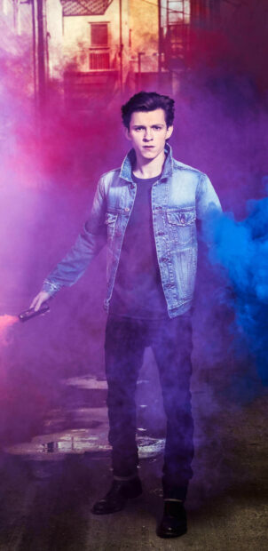 Tom Holland wearing a denim jacket standing in colorful smoke holding a flare