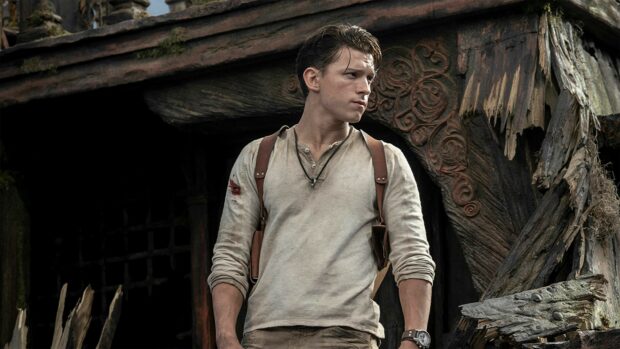 Tom Holland standing in rugged outfit with leather straps in front of a wooden carved background