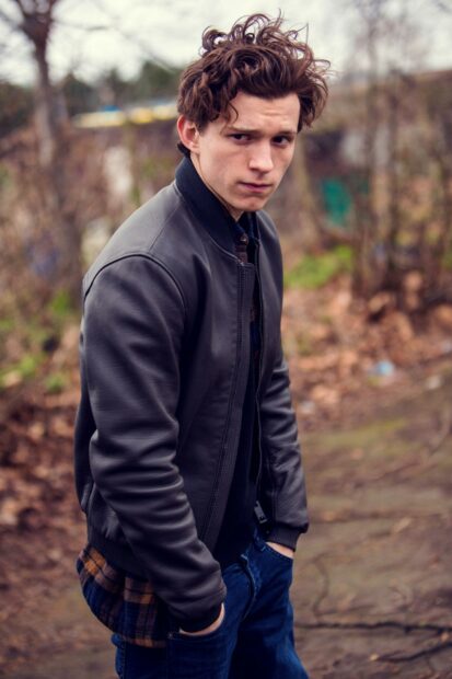 Tom Holland wearing a leather jacket standing outdoors with a serious expression