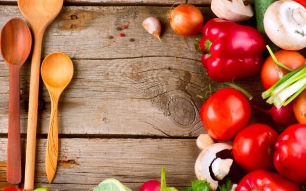 Fresh tomatoes and vegetables arranged on a wooden surface with wooden spoons nearby