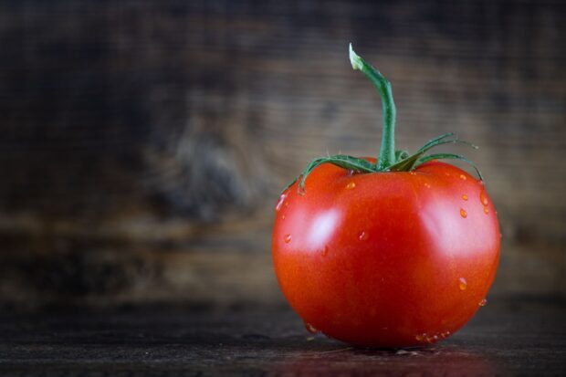 Fresh tomato with green stem and water droplets on wooden surface