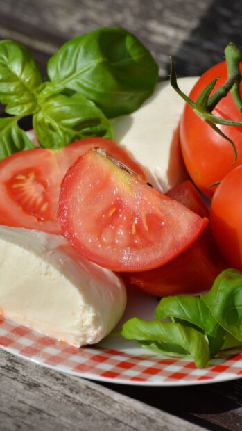 Fresh tomato slices with basil leaves and mozzarella cheese on a plate