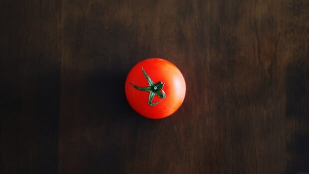 A fresh tomato with green stem on a dark wooden surface
