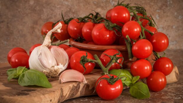 A bunch of fresh tomato with garlic and basil on a wooden surface