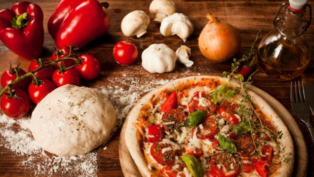 Fresh tomato ingredients with pizza dough and herbs on wooden table