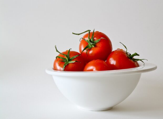 Fresh tomatoes with green stems in a white bowl on a plain background